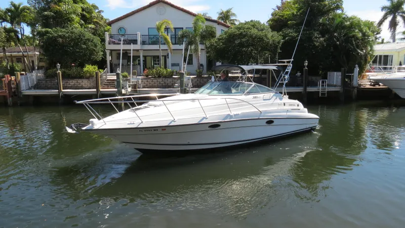 Slide: The Image of 1998 Doral 300 SC V Drive boat on a calm canal, with a house and palm trees in the background. - 2