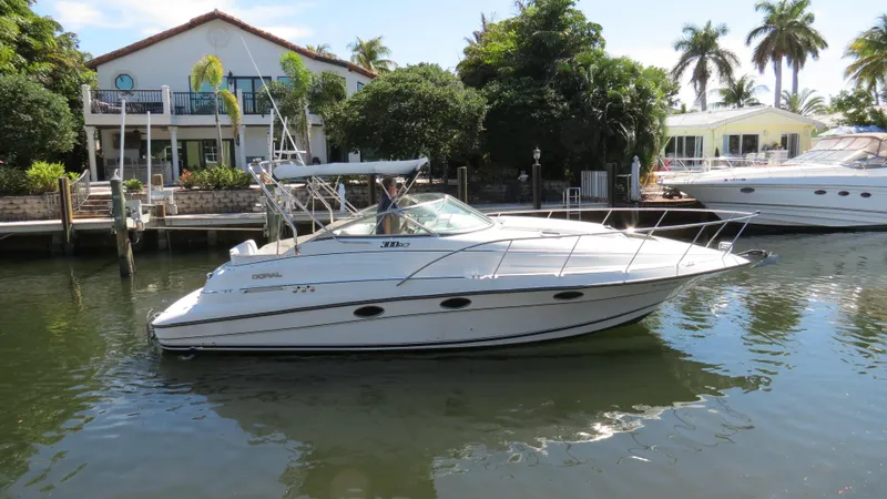 Slide: The Image of 1998 Doral 300 SC V Drive boat docked near waterfront homes with palm trees. - 6