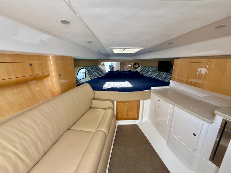 Slide: The Image of 2013 Intrepid 390 Sport Yacht interior with beige seating, wooden cabinets, and a cozy bed. - 18