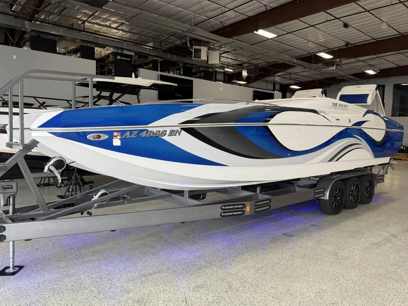 The Image of 2008 Magic 30' Sceptor boat with blue and white design on a trailer in a showroom. - 1