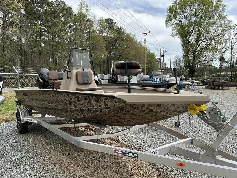 Slide: The Image of 2025 Excel Bay Pro 203 Elite boat on trailer, camo design, parked outdoors. - 1