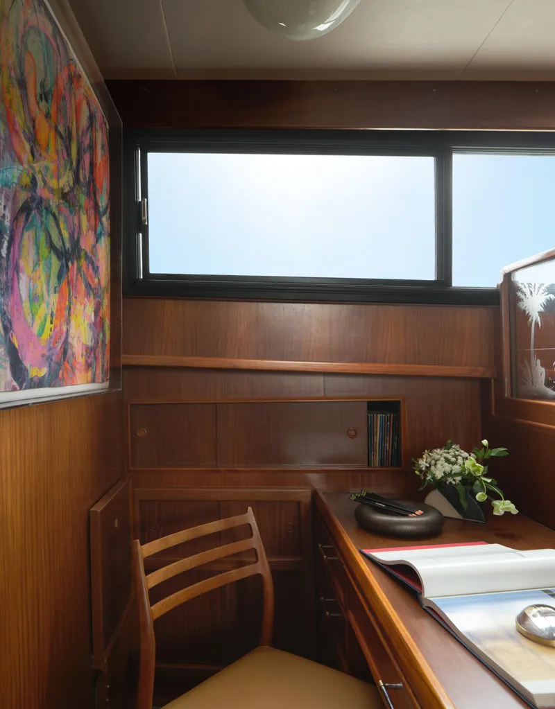 Slide: The Image of 1981 Hatteras Motor Yacht interior with wooden desk, chair, colorful artwork, and window view. - 18