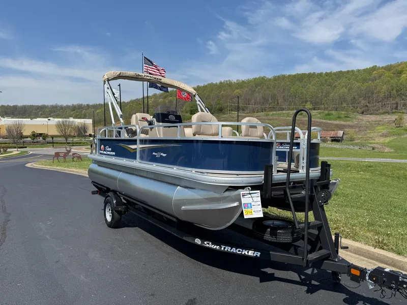 Slide: The Image of 2025 Sun Tracker Bass Buggy 18 DLX pontoon boat on trailer, parked outdoors. - 2