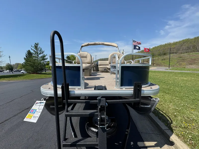 Slide: The Image of 2025 Sun Tracker Bass Buggy 18 DLX pontoon boat on trailer, flags waving, sunny day. - 3