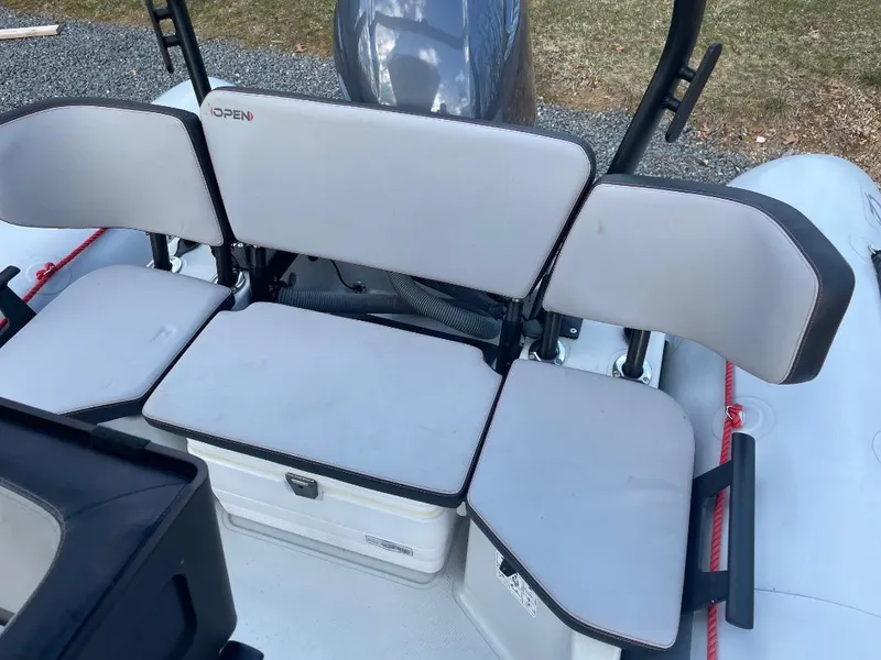 Slide: The Image of 2020 Zodiac Open 6.5 boat seating area with cushioned seats and storage compartment. - 6