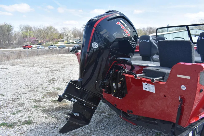 Slide: The Image of 2025 Lund 1775 Impact XS Sport boat with powerful outboard motor on gravel surface. - 6