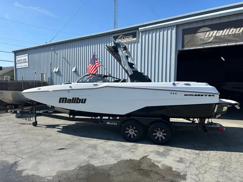 Slide: The Image of 2025 Malibu 23 MXZ boat on trailer outside dealership, featuring sleek design and American flag. - 2