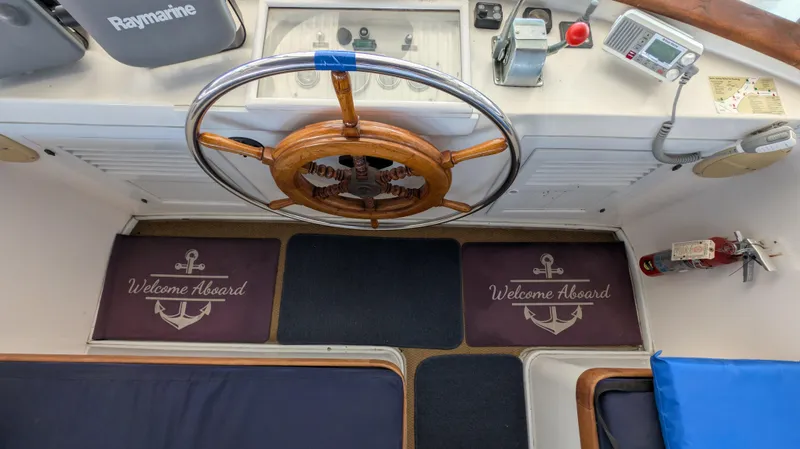 Slide: The Image of 1982 Monk 36 boat helm with wooden wheel, nautical mats, and navigation equipment. - 23