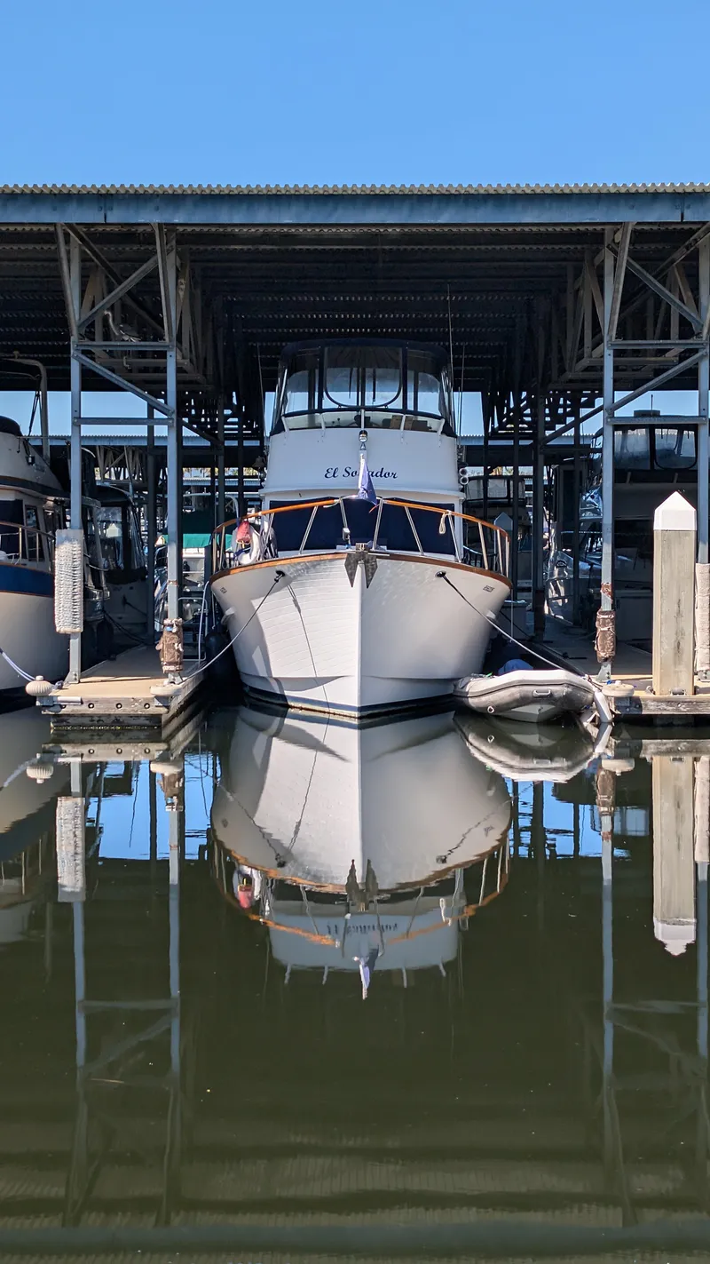 Slide: The Image of 1982 Monk 36 boat docked in marina, reflecting on calm water under a clear blue sky. - 6
