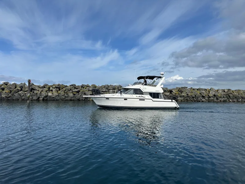Slide: The Image of 1994 Carver 370 Voyager yacht on calm water with rocky shoreline and cloudy sky. - 3