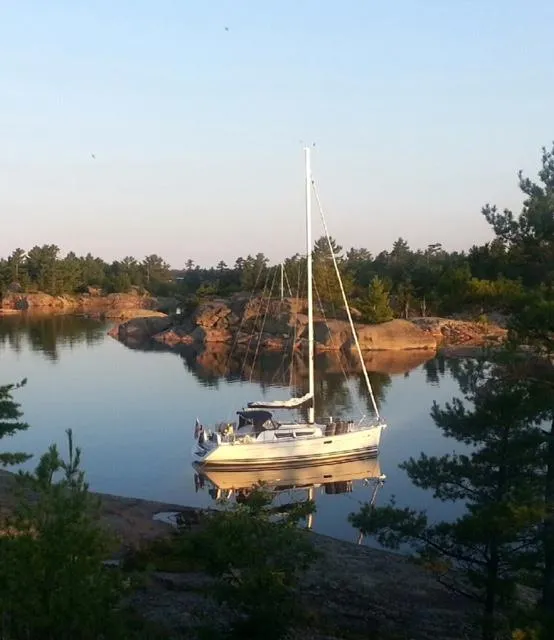 Slide: The Image of Jeanneau Sun Odyssey 36i sailboat anchored in a serene, rocky cove, surrounded by trees. - 4