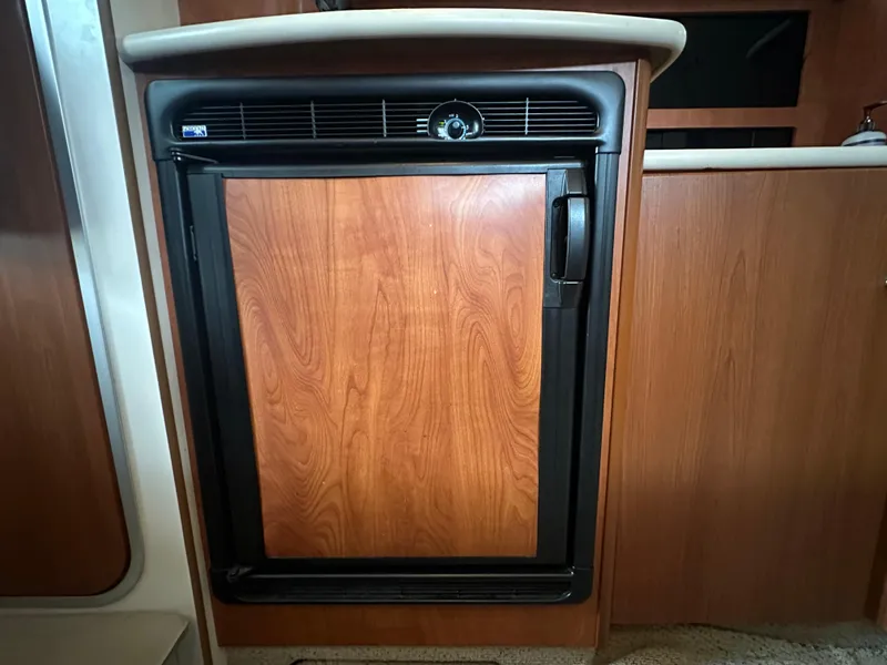 Slide: The Image of 2005 Bayliner 305 interior with a wooden panel refrigerator in the kitchen area. - 25