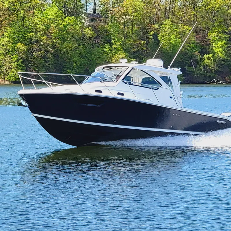Slide: The Image of 2023 Pursuit OS 325 Offshore boat cruising on a serene lake with lush green trees. - 2