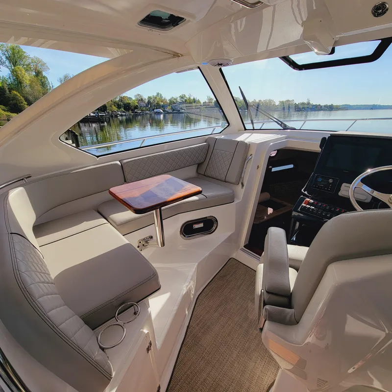 Slide: The Image of 2023 Pursuit OS 325 Offshore boat interior with seating, table, and helm, overlooking serene waters. - 24