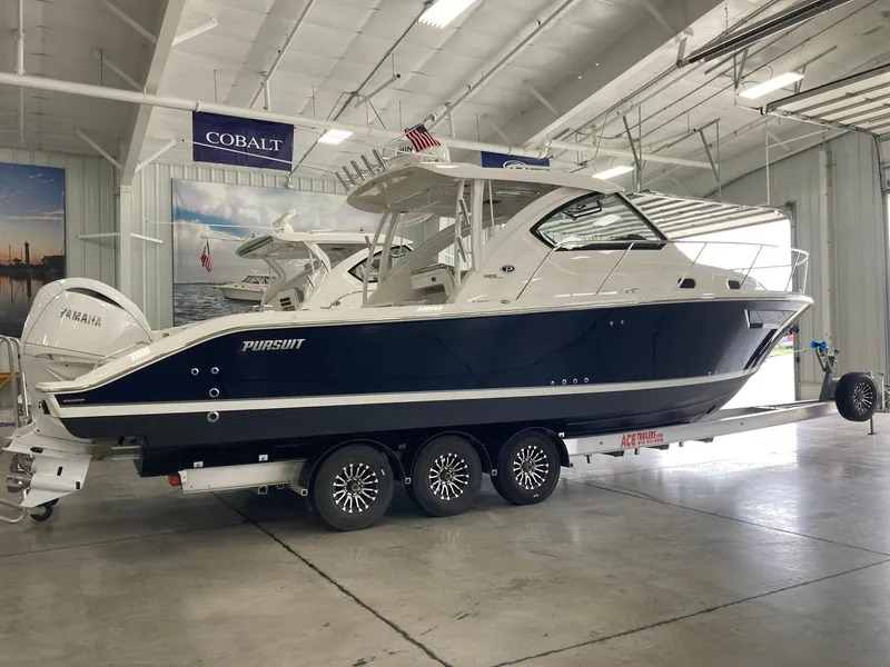 Slide: The Image of 2023 Pursuit OS 325 Offshore boat in showroom, featuring sleek design and triple-axle trailer. - 4