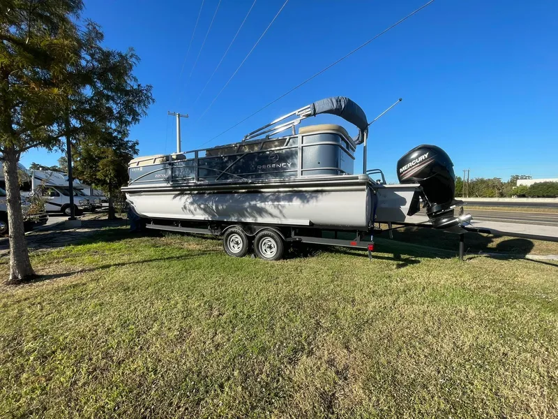 Slide: The Image of 2017 Regency 220 DL3 pontoon boat on trailer, parked on grass under clear blue sky. - 3