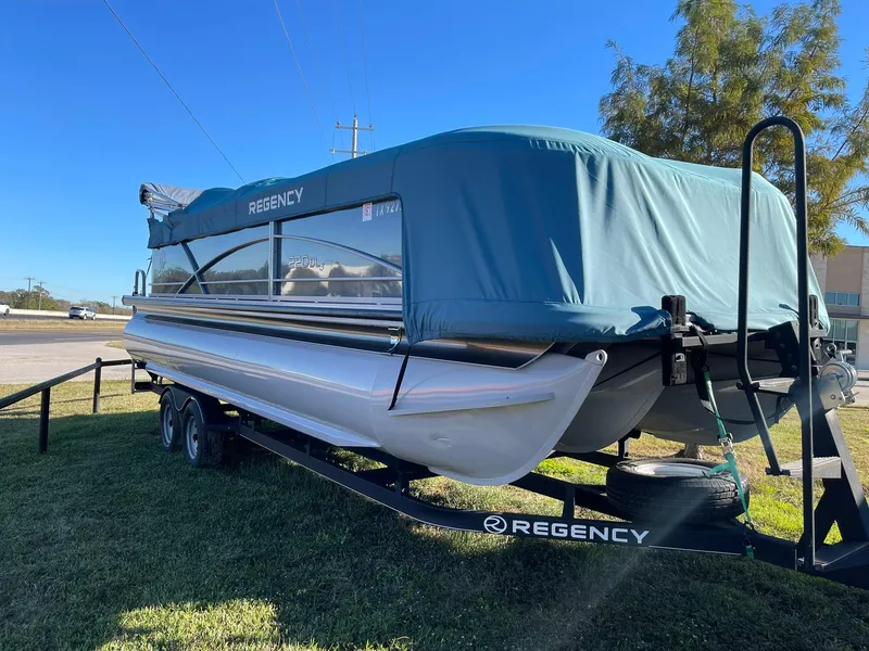 Slide: The Image of 2017 Regency 220 DL3 pontoon boat on trailer with blue cover, parked on grass. - 37