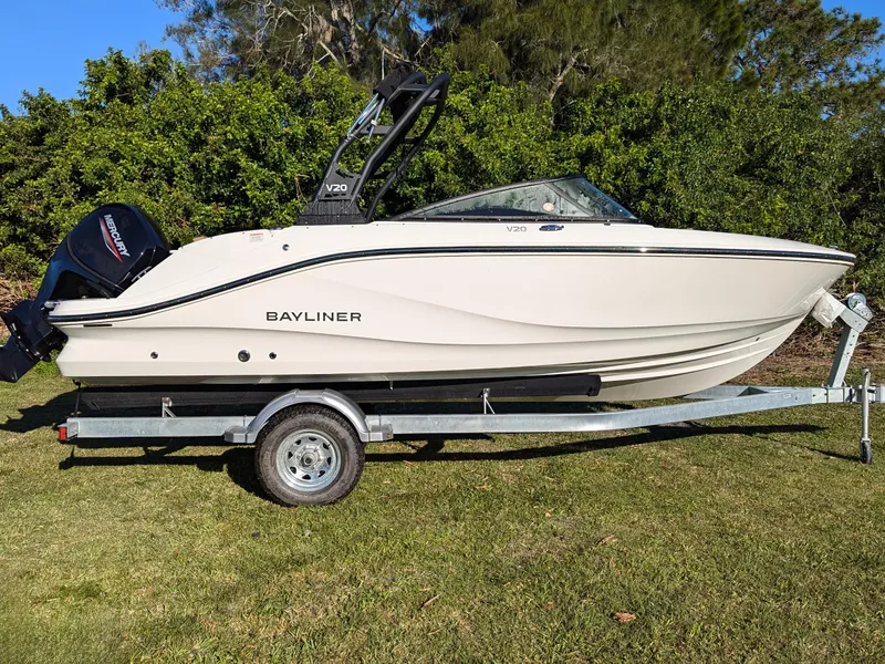Slide: The Image of 2025 Bayliner V20 boat on trailer, parked on grass with trees in background. - 2