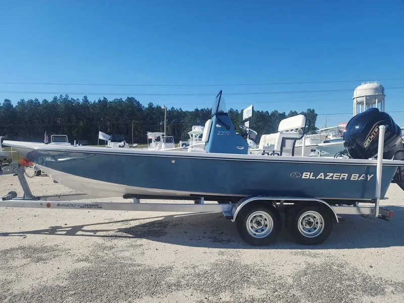 Slide: The Image of 2025 Blazer Bay 2200 boat on trailer, parked outdoors under clear blue sky. - 2