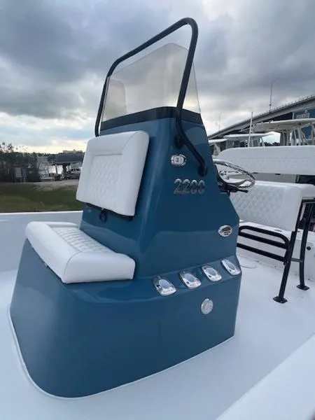 Slide: The Image of 2025 Blazer Bay 2200 boat console with blue and white seating, under cloudy sky. - 6