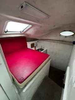 Slide: The Image of 2004 Baha Cruisers 290 King Kat cabin interior with red bedding and compact kitchenette. - 24