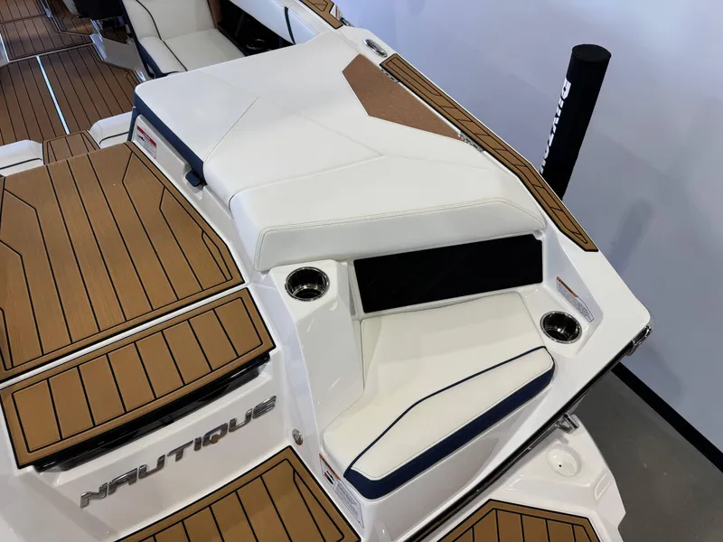 Slide: The Image of 2025 Nautique Super Air Nautique S23 boat interior with teak flooring and white seating. - 10