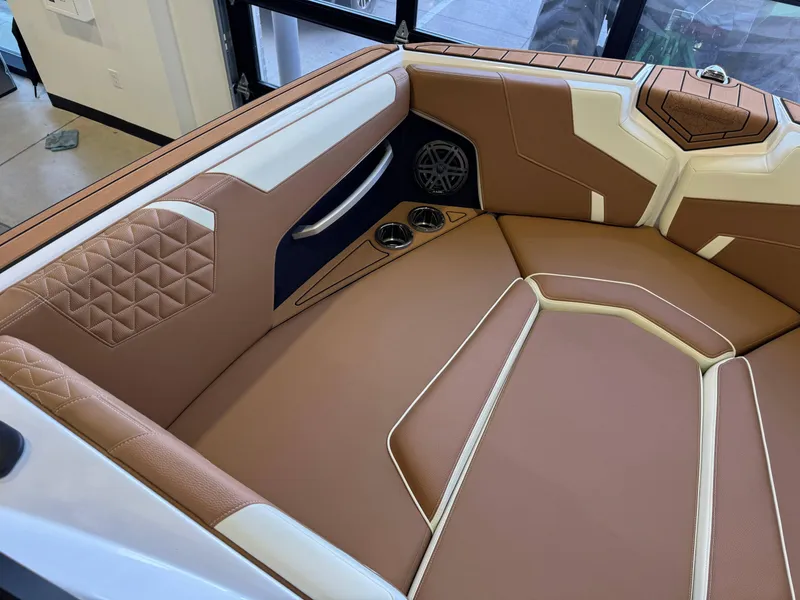 Slide: The Image of 2025 Nautique Super Air Nautique GS24 interior with tan and white upholstery, featuring cup holders and speaker. - 19
