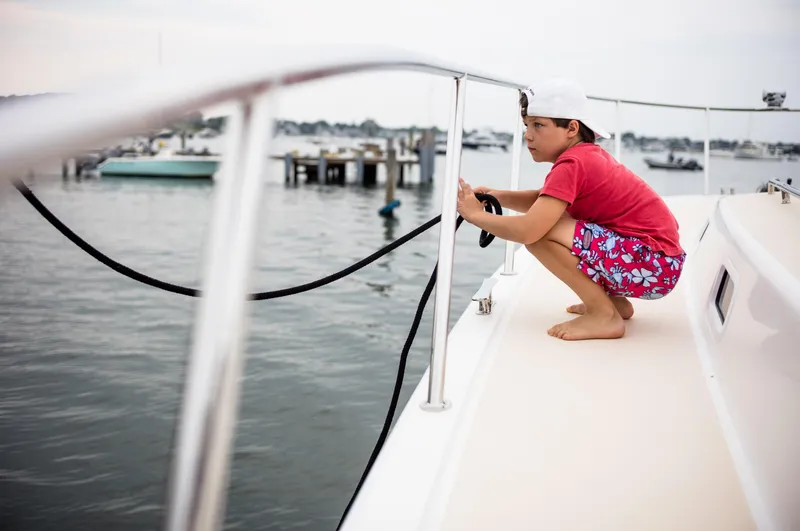 Slide: The Image of Boy on MJM 53z boat holding rope, wearing red shirt and shorts, near marina. - 7