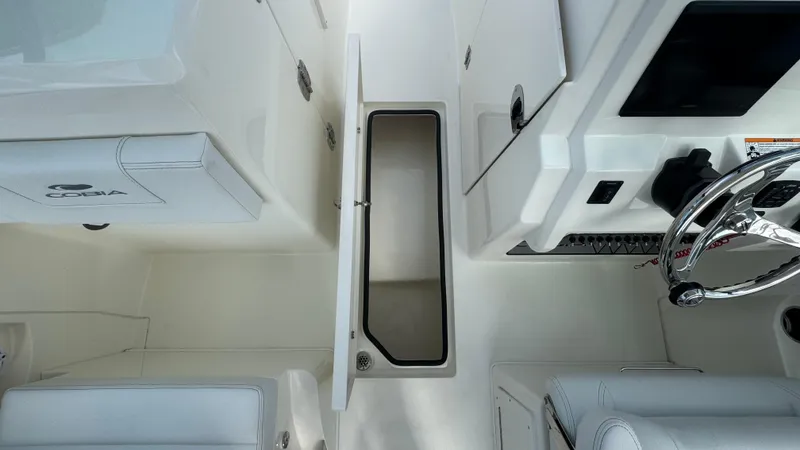 Slide: The Image of 2025 Cobia 240 Dual Console boat interior with open storage compartment and steering wheel. - 28