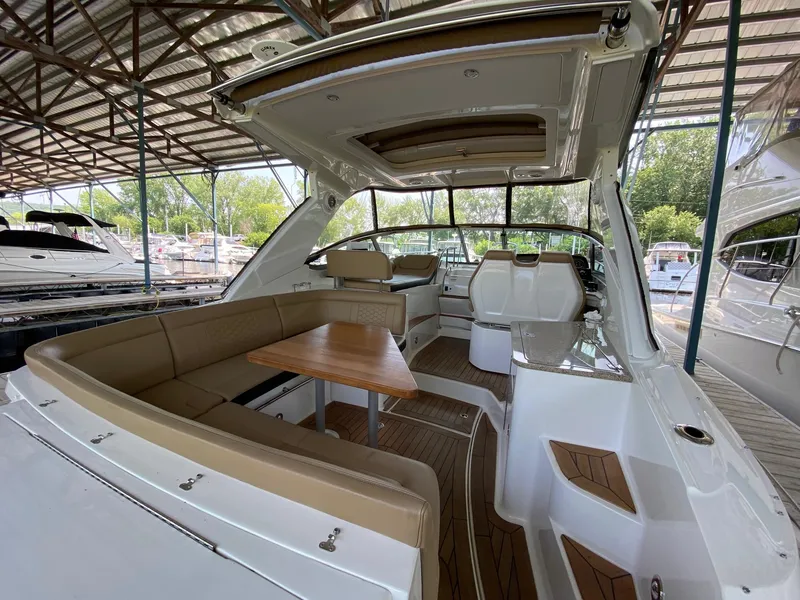 Slide: The Image of 2018 Sea Ray Sundancer 350 interior with seating, table, and helm under a covered dock. - 11