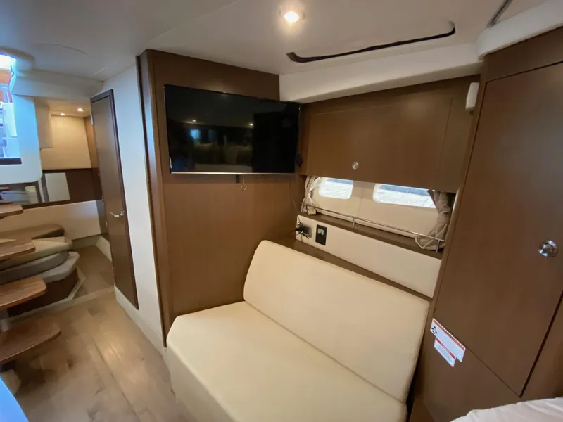 Slide: The Image of 2018 Sea Ray Sundancer 350 interior with beige seating, TV, and wooden cabinetry. - 35