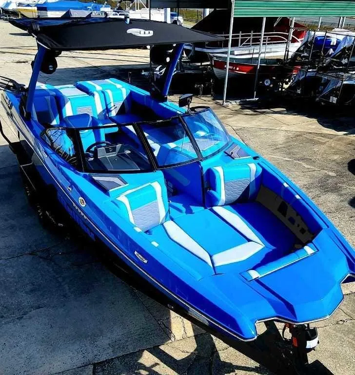 Slide: The Image of 2024 Malibu Wakesetter 23 MXZ boat with blue and white seating, docked outdoors. - 18