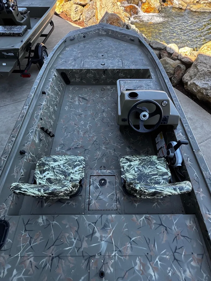 Slide: The Image of 2025 Tracker Grizzly 1754 SC boat with camouflage seats and steering console, near water and rocks. - 3