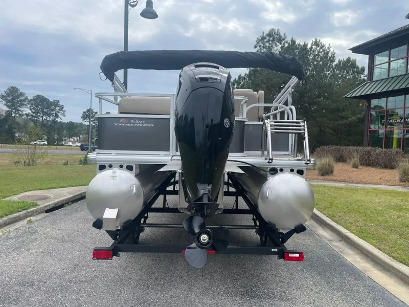 Slide: The Image of 2025 Sun Tracker Party Barge 18 DLX pontoon boat, rear view, parked outdoors. - 4