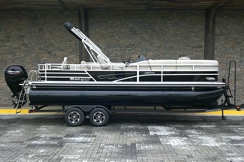 The Image of 2025 Ranger Reata 220FC pontoon boat on trailer, parked against stone wall. - 0