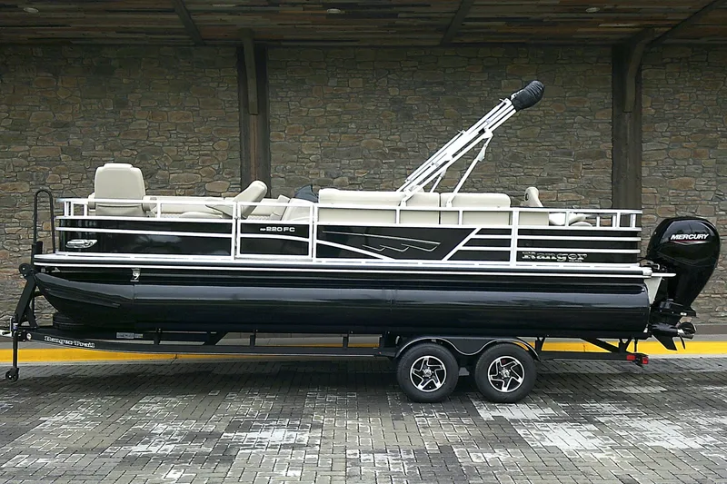 Slide: The Image of 2025 Ranger Reata 220FC pontoon boat on trailer, parked against stone wall. - 1