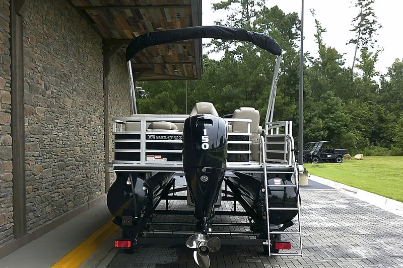 Slide: The Image of 2025 Ranger Reata 220FC boat with outboard motor, parked near stone wall and greenery. - 3