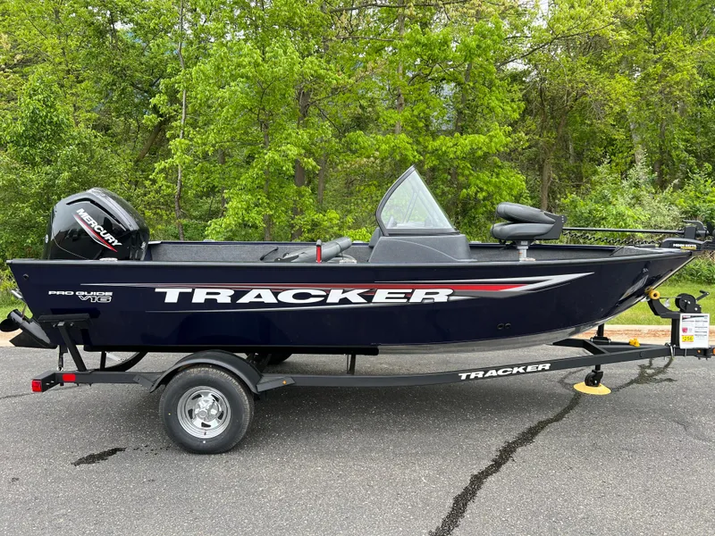 Slide: The Image of 2025 Tracker Pro Guide V-16 WT boat on trailer, parked on asphalt with green trees in background. - 3