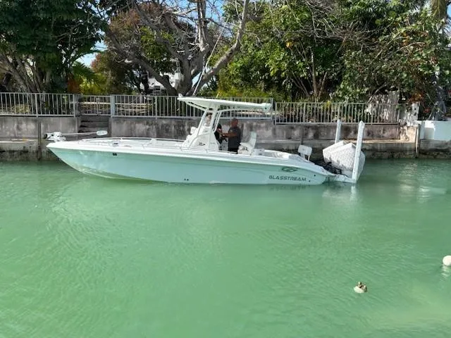 Slide: The Image of 2023 Glasstream 280 Pro-XS boat on calm green water near a tree-lined shore. - 24