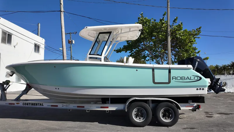 Slide: The Image of 2025 Robalo R250 boat on trailer, light blue hull, parked outdoors. - 1