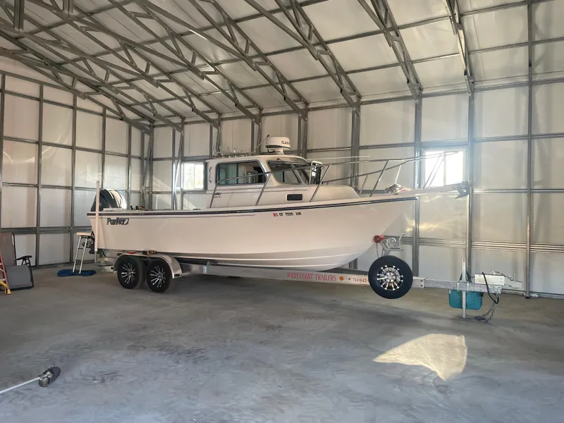Slide: The Image of 2024 Parker 2320 Sport Cabin boat on trailer inside a spacious metal garage. - 0
