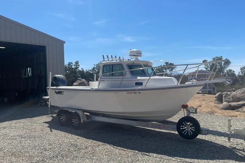 Slide: The Image of 2024 Parker 2320 Sport Cabin boat on trailer, parked outside a garage. - 1