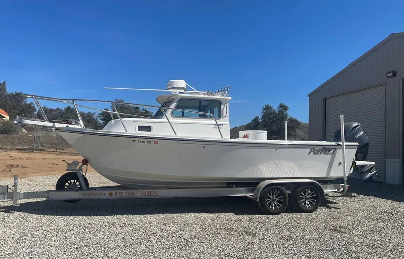 Slide: The Image of 2024 Parker 2320 Sport Cabin boat on trailer, parked outdoors near a building. - 2