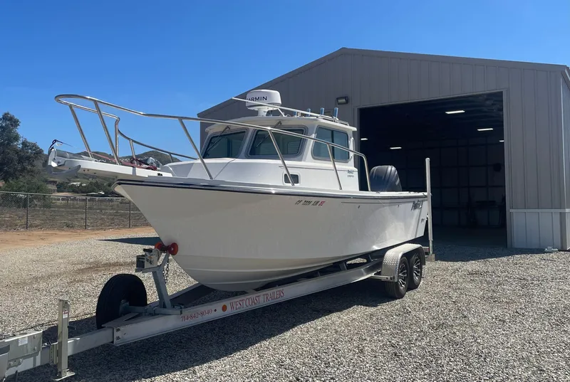 Slide: The Image of 2024 Parker 2320 Sport Cabin boat on trailer outside a large garage. - 7