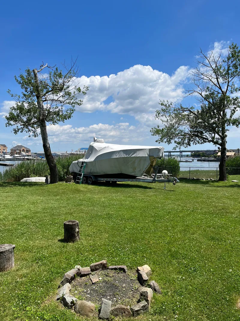 Slide: The Image of 2000 Pursuit 2860 Denali boat covered on grassy shore, with trees and water in the background. - 25