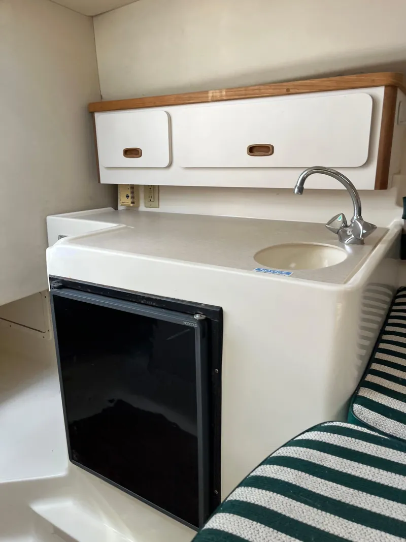 Slide: The Image of 2000 Pursuit 2860 Denali boat interior with kitchenette, sink, and striped seating. - 8