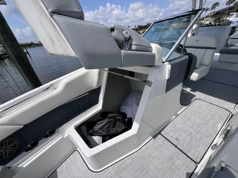 Slide: The Image of 2019 Cobalt 25 SC boat interior with storage compartment, gray seating, and waterfront view. - 20