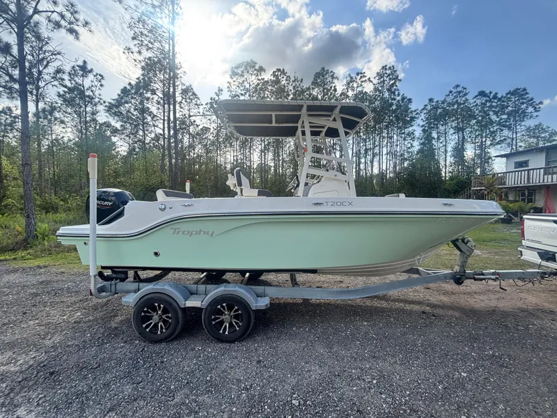 Slide: The Image of 2022 Bayliner Trophy T20CX boat on trailer, parked outdoors with trees in background. - 8