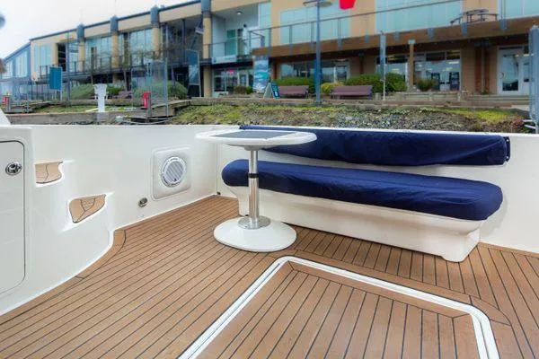Slide: The Image of 2005 Sea Ray 520 Sedan Bridge yacht deck with seating and table, docked near modern buildings. - 12