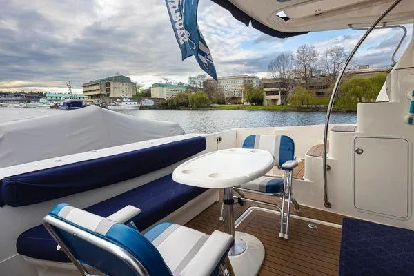 Slide: The Image of 2005 Sea Ray 520 Sedan Bridge yacht deck with seating and table, overlooking a scenic waterfront. - 16